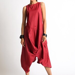 May include: A red sleeveless jumpsuit with a loose, flowing fit. The jumpsuit has a wide leg and a low, scoop neckline. The model is wearing black ankle boots.