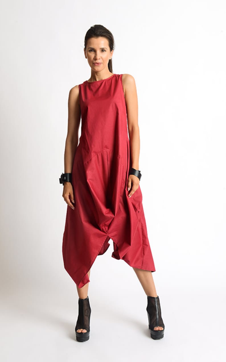 May include: A red sleeveless jumpsuit with a loose, flowing fit. The jumpsuit has a wide leg and a low, scoop neckline. The model is wearing black ankle boots.