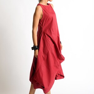 Peut inclure: Une robe rouge sans manches avec une silhouette ample et fluide. La robe a un col rond simple et une jupe l&eacute;g&egrave;rement pliss&eacute;e. Le mannequin porte des sandales compens&eacute;es &agrave; plateforme noires.