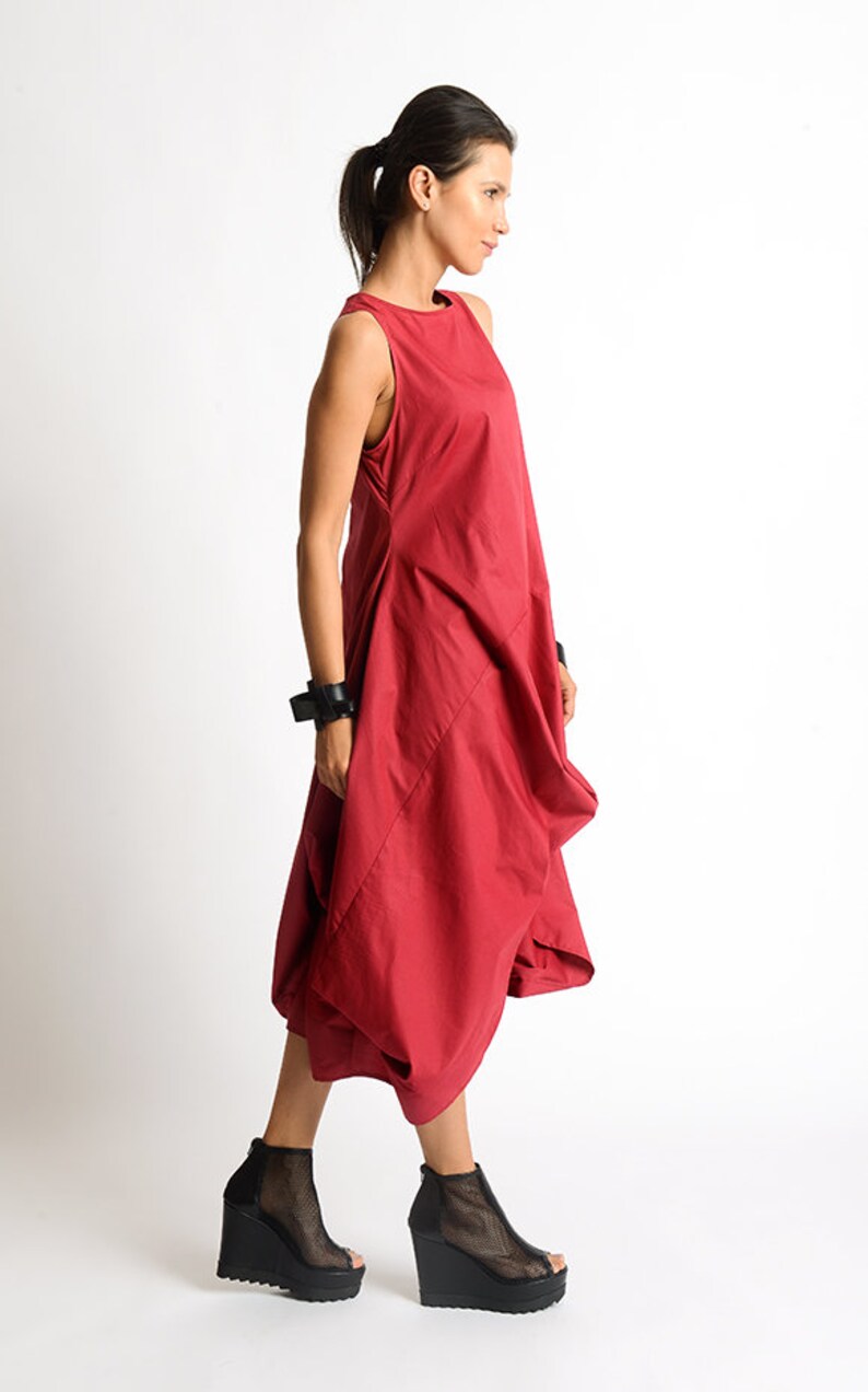 Peut inclure: Une robe rouge sans manches avec une silhouette ample et fluide. La robe a un col rond simple et une jupe l&eacute;g&egrave;rement pliss&eacute;e. Le mannequin porte des sandales compens&eacute;es &agrave; plateforme noires.