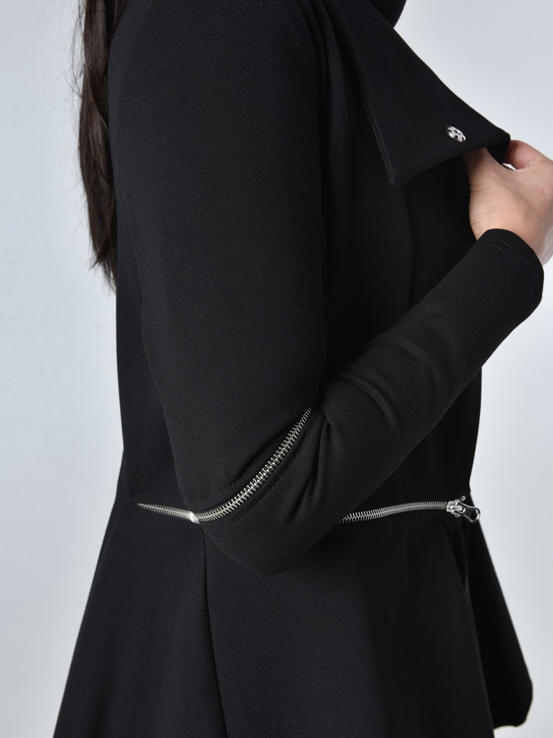 Puede incluir: Chaqueta negra de manga larga con un detalle de cremallera en las mangas y un cuello que se puede llevar subido o bajado.