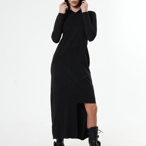 May include: A black long-sleeved hooded dress with a diagonal seam detail and a high slit on the side. The dress is worn with black combat boots.