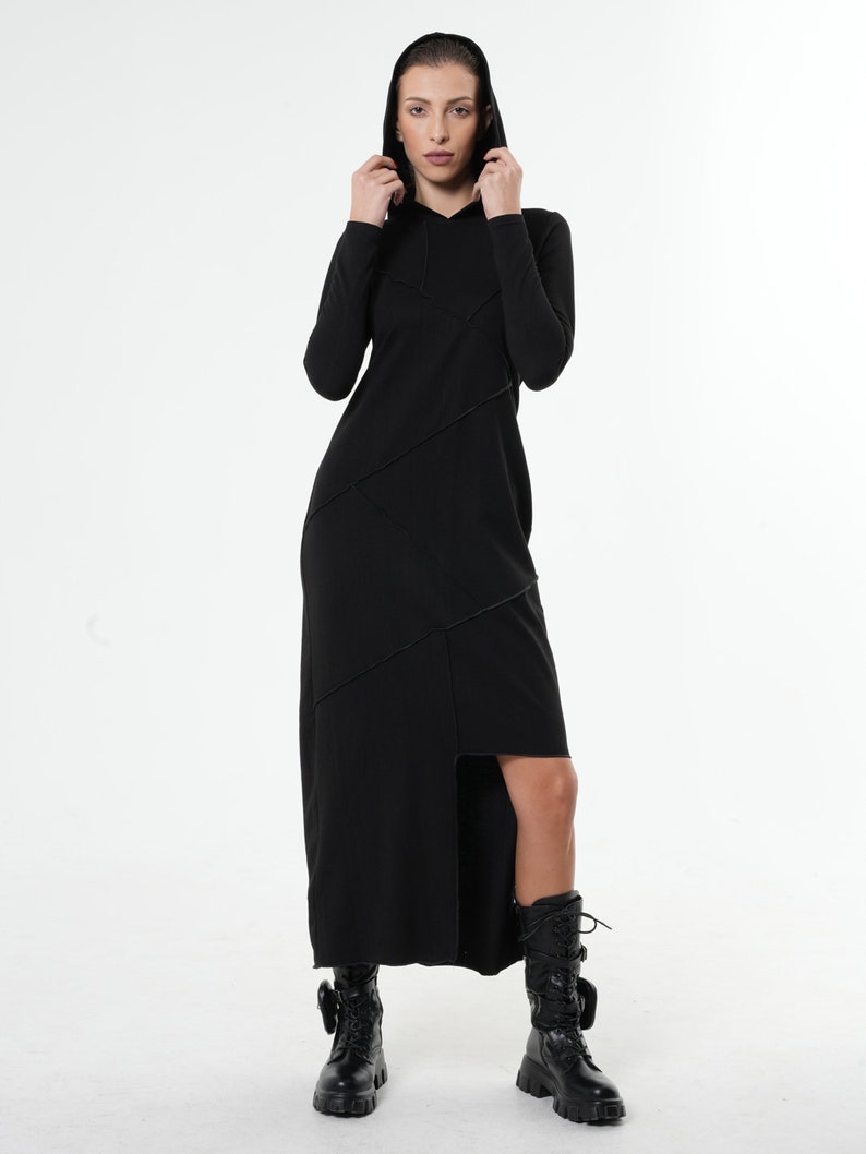May include: A black long-sleeved hooded dress with a diagonal seam detail and a high slit on the side. The dress is worn with black combat boots.