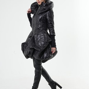 May include: A black puffer jacket with a large, dramatic collar and a fitted silhouette. The jacket has a zip closure and a quilted design.