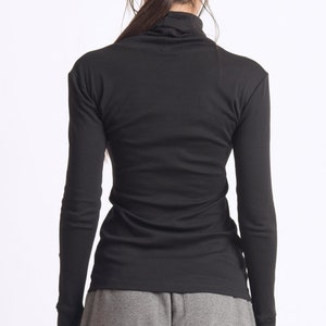 May include: A black long-sleeved shirt with a mock neck. The shirt is fitted and has a slightly longer length in the back. The model is wearing gray pants.