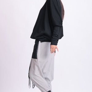 May include: A black long-sleeve top and light gray pants with black accents. The pants have a unique design with a black panel and drawstring detail. Black platform sneakers complete the outfit. Fashion apparel.