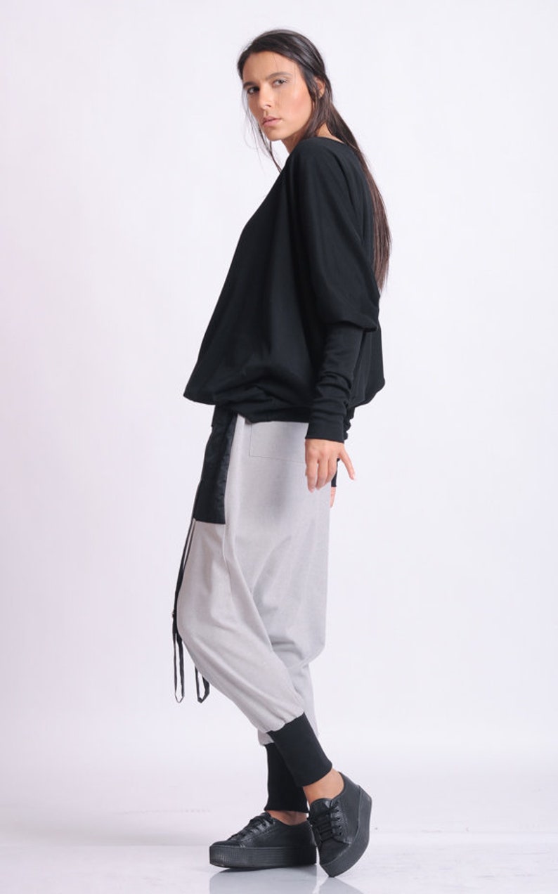 May include: A black long-sleeve top and light gray pants with black accents. The pants have a unique design with a black panel and drawstring detail. Black platform sneakers complete the outfit. Fashion apparel.