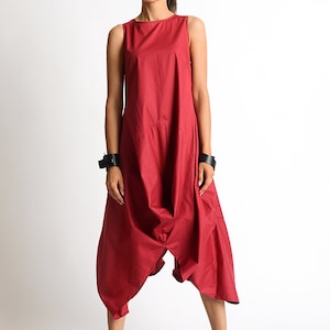 Peut inclure: Une combinaison rouge sans manches &agrave; la coupe ample et fluide. La combinaison a une jambe large et une taille fronc&eacute;e. Le mannequin porte des bottines noires &agrave; la cheville.
