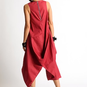 Peut inclure: Une combinaison rouge sans manches avec une longue fermeture &eacute;clair dans le dos. La combinaison a un design unique et asym&eacute;trique avec une jupe fluide et drap&eacute;e.