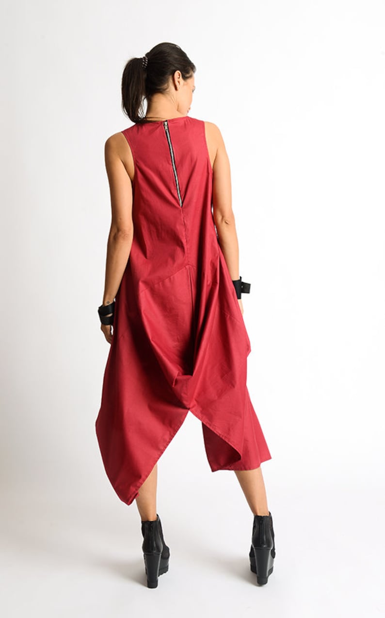 Peut inclure: Une combinaison rouge sans manches avec une longue fermeture &eacute;clair dans le dos. La combinaison a un design unique et asym&eacute;trique avec une jupe fluide et drap&eacute;e.