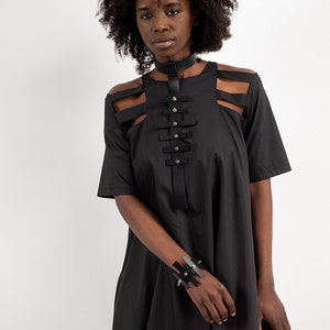 May include: A black dress with cutouts at the shoulders and a leather choker and bracelet with silver accents.