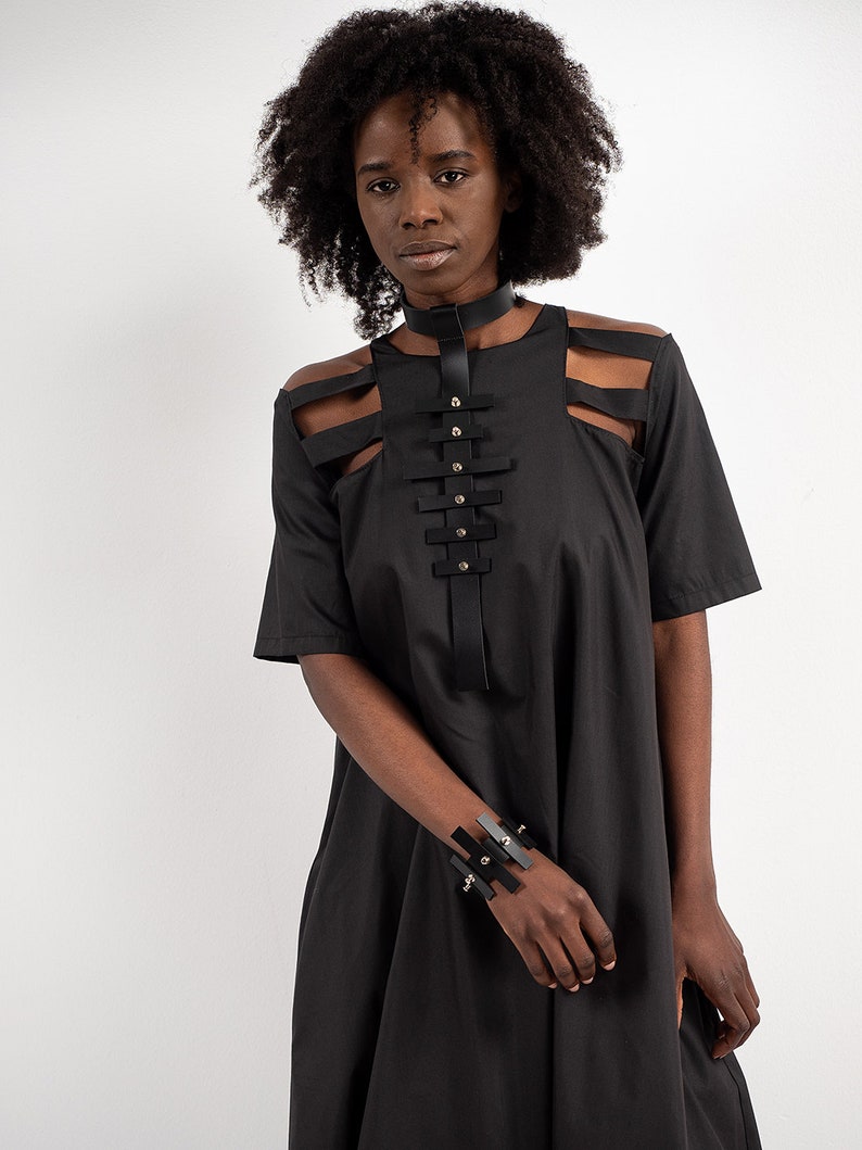 May include: A black dress with cutouts at the shoulders and a leather choker and bracelet with silver accents.