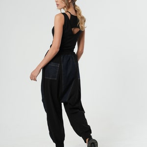 May include: A woman wearing a black tank top with a cut-out back and black and blue denim pants.