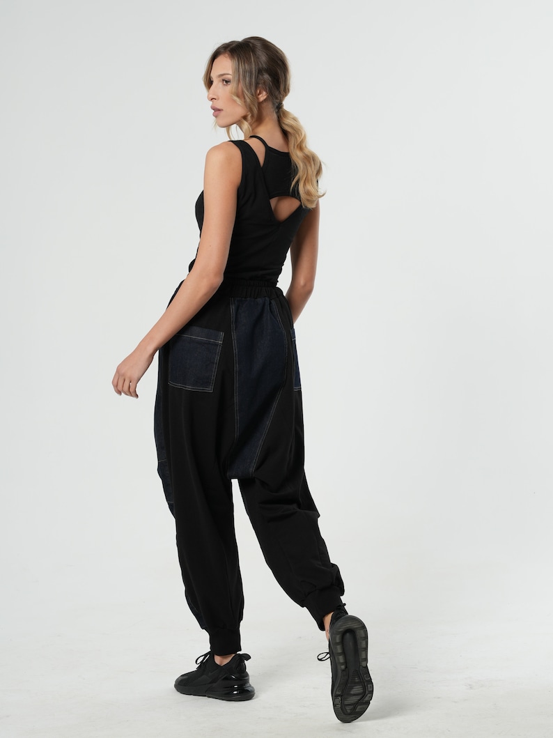 May include: A woman wearing a black tank top with a cut-out back and black and blue denim pants.