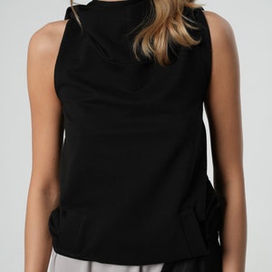 May include: A black sleeveless top with a mock neck and a gathered detail at the bottom.
