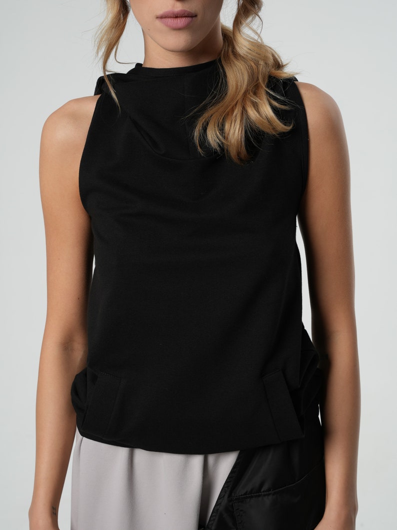 May include: A black sleeveless top with a mock neck and a gathered detail at the bottom.
