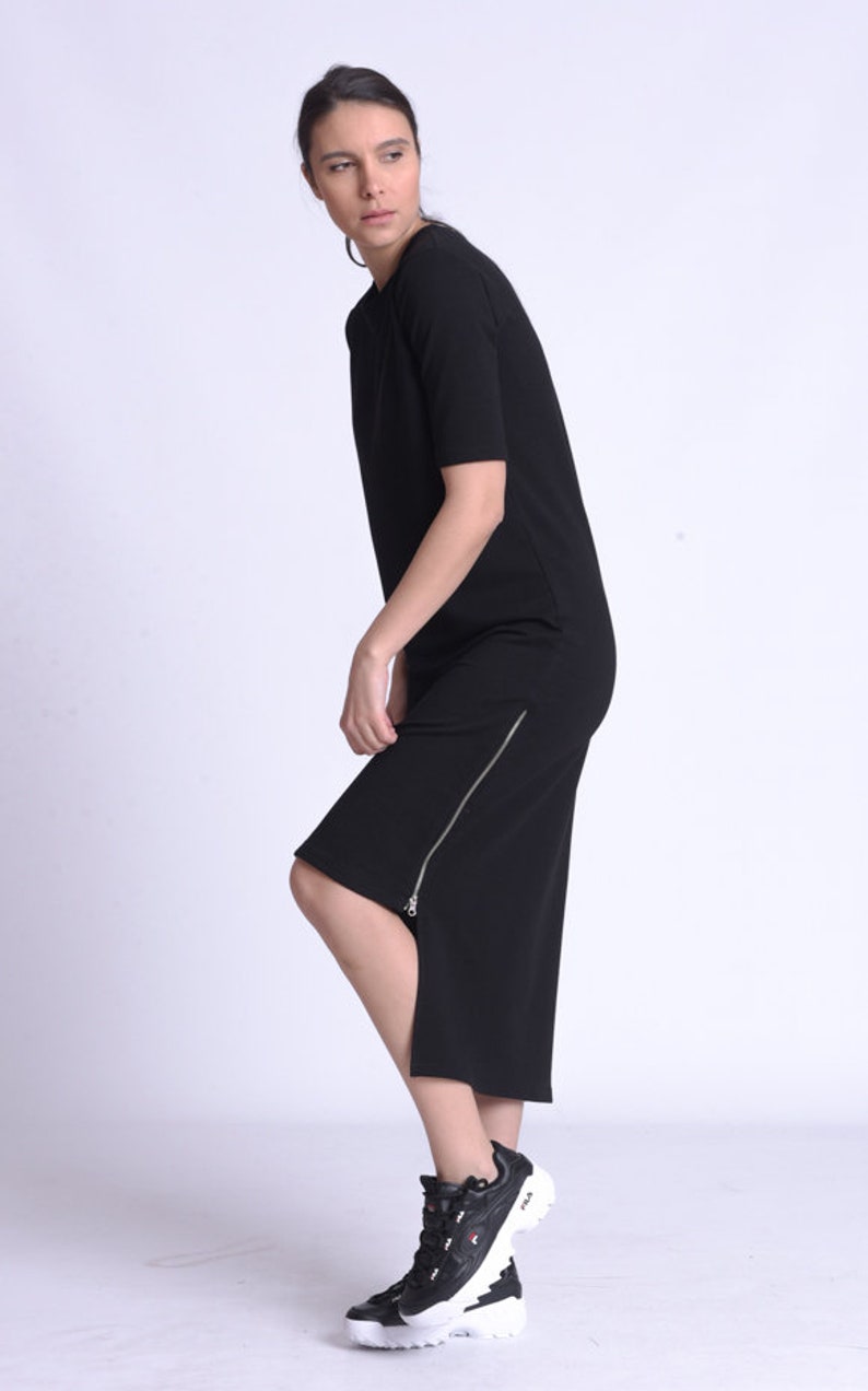 Puede incluir: Un vestido midi negro con cremallera lateral y mangas cortas. El vestido est&aacute; hecho de una tela suave y el&aacute;stica. La modelo lleva zapatillas negras y blancas.