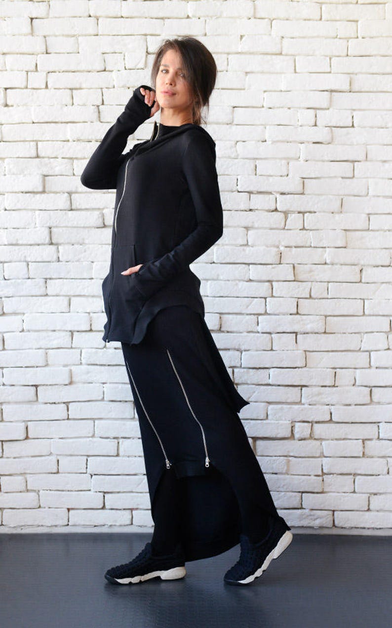 May include: A black hooded sweatshirt with a long, asymmetrical skirt. The skirt has multiple zippers down the front. The model is wearing white sneakers.
