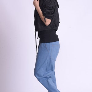 May include: A woman wearing a black hooded jacket, a black shirt, blue jeans, and black sneakers with white accents. The sneakers have the word "FILA" on the side.