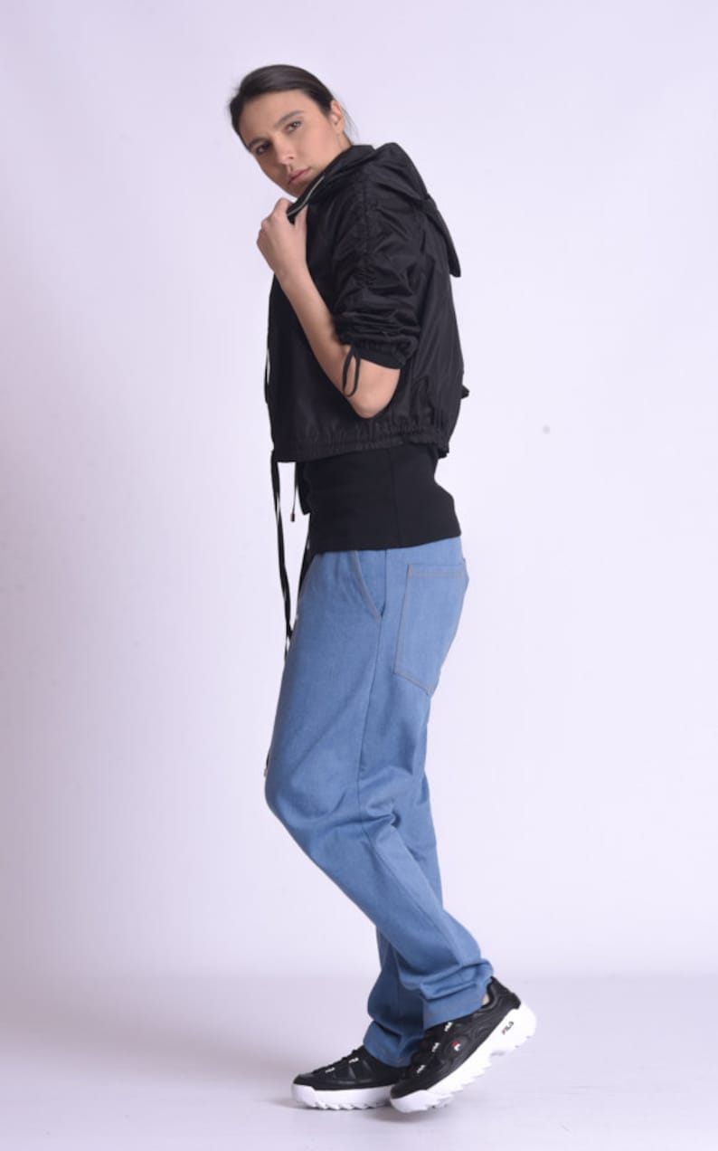May include: A woman wearing a black hooded jacket, a black shirt, blue jeans, and black sneakers with white accents. The sneakers have the word "FILA" on the side.