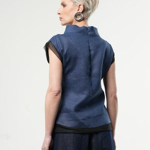 May include: A blue linen top with a black mesh trim and a high neckline. The top has short sleeves and a relaxed fit.