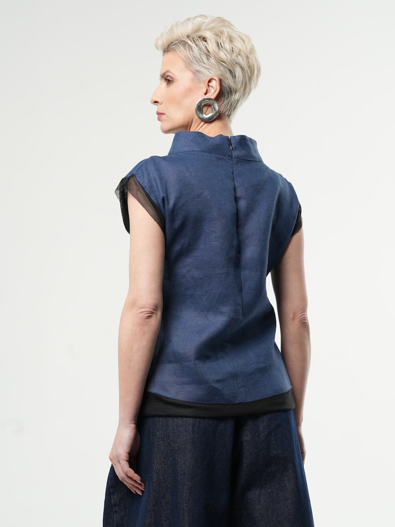 May include: A blue linen top with a black mesh trim and a high neckline. The top has short sleeves and a relaxed fit.
