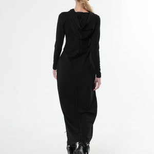 May include: A black long-sleeved maxi dress with a hood. The dress has a fitted bodice and a flowing skirt. The model is wearing black boots.