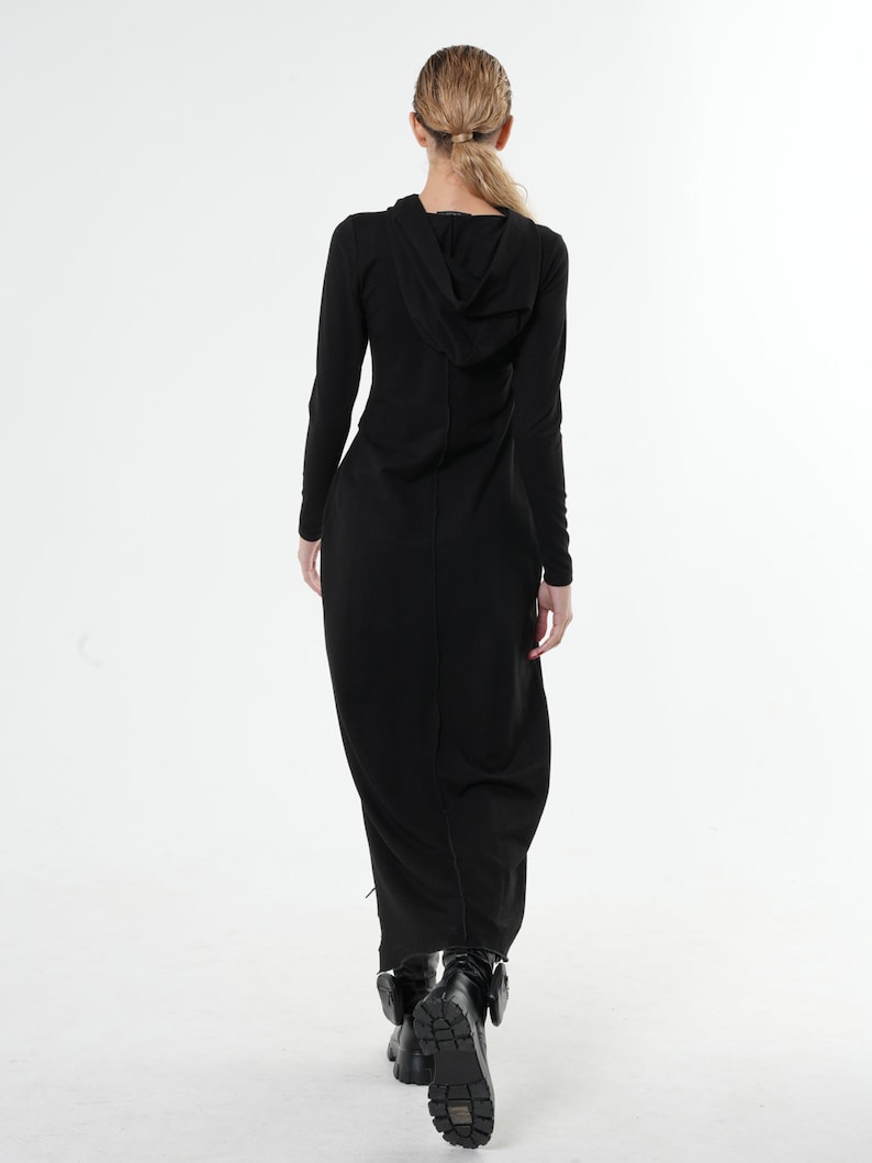 May include: A black long-sleeved maxi dress with a hood. The dress has a fitted bodice and a flowing skirt. The model is wearing black boots.