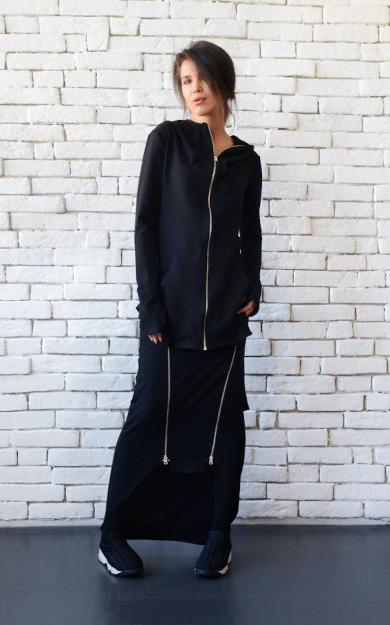 May include: A black long-sleeved hooded top with a zipper closure and a matching black skirt with zipper details. The model is wearing black sneakers.