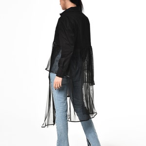 May include: A black long-sleeved shirt with a sheer overlay and a high-low hemline. The shirt is worn with blue jeans.