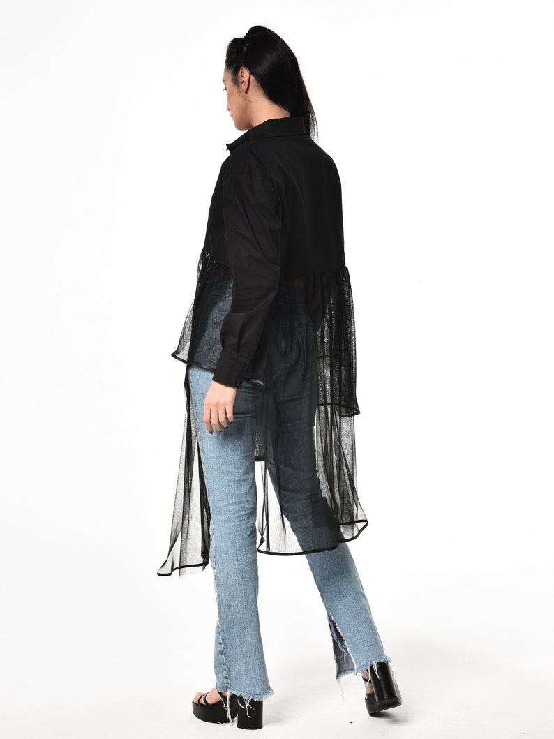 May include: A black long-sleeved shirt with a sheer overlay and a high-low hemline. The shirt is worn with blue jeans.