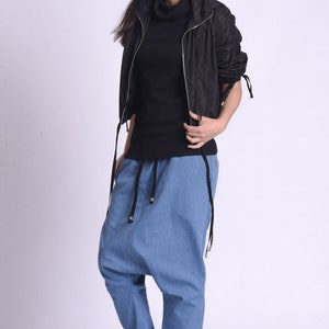 May include: A woman wearing a black hooded jacket, a black turtleneck shirt, blue denim pants with a drawstring waist, and black and white sneakers.