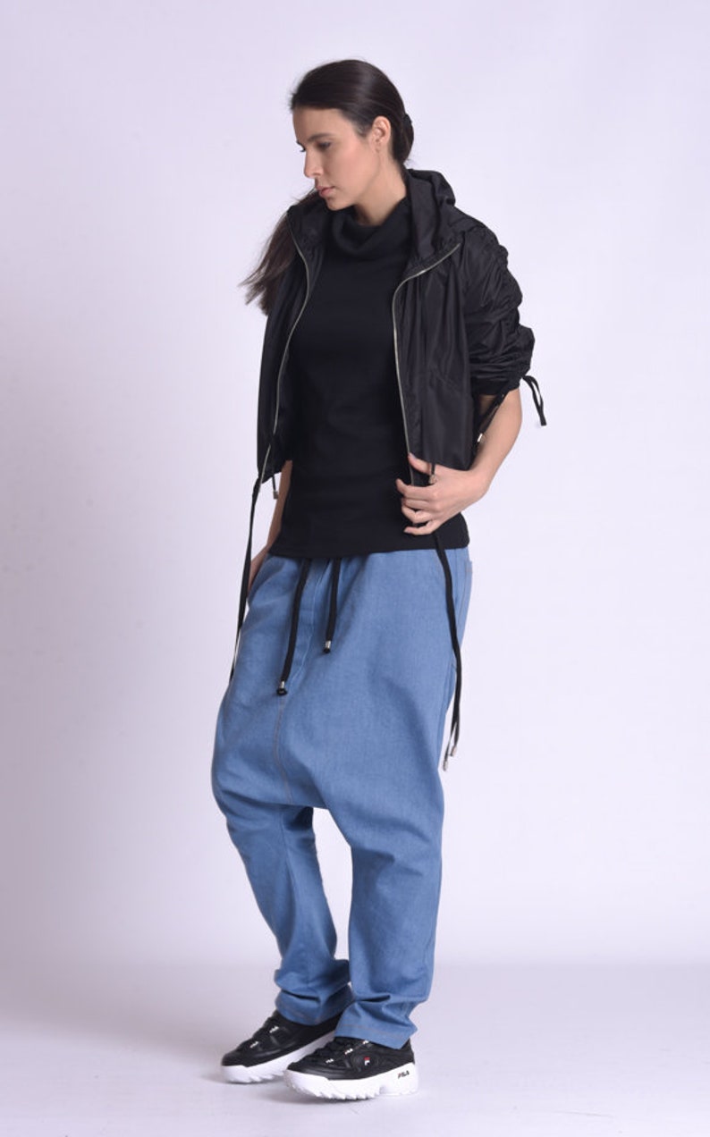 May include: A woman wearing a black hooded jacket, a black turtleneck shirt, blue denim pants with a drawstring waist, and black and white sneakers.
