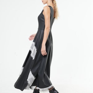 May include: A black maxi dress with white lace trim. The dress has a sleeveless design and a flowing skirt. The model is wearing black heeled boots.