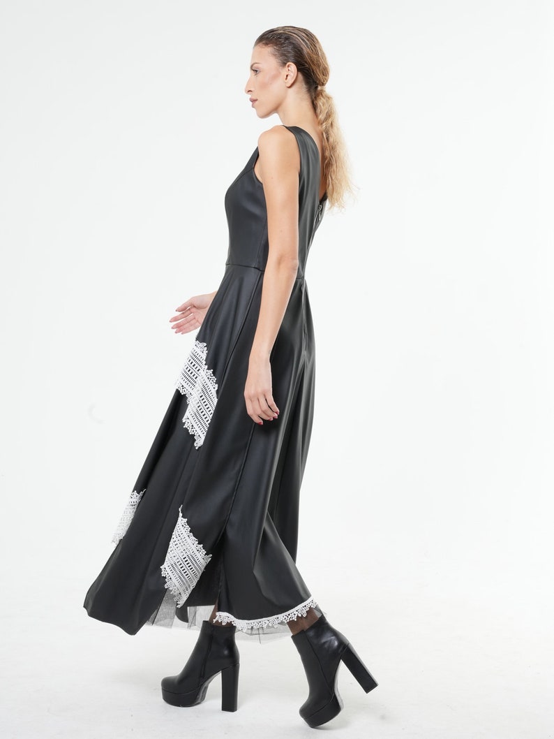 May include: A black maxi dress with white lace trim. The dress has a sleeveless design and a flowing skirt. The model is wearing black heeled boots.