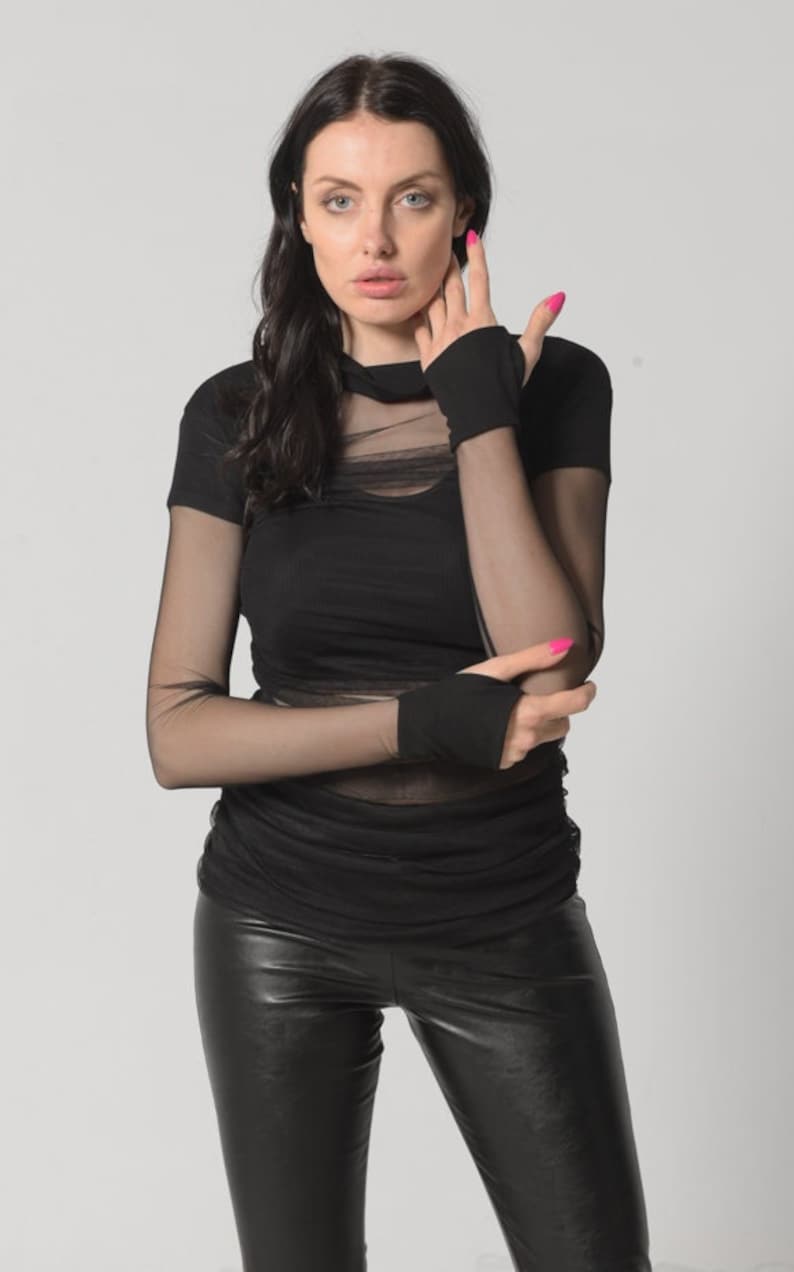 May include: A woman wearing a black mesh top with a black turtleneck and black leather trousers. She is wearing black fingerless gloves and has pink nail polish on her nails.