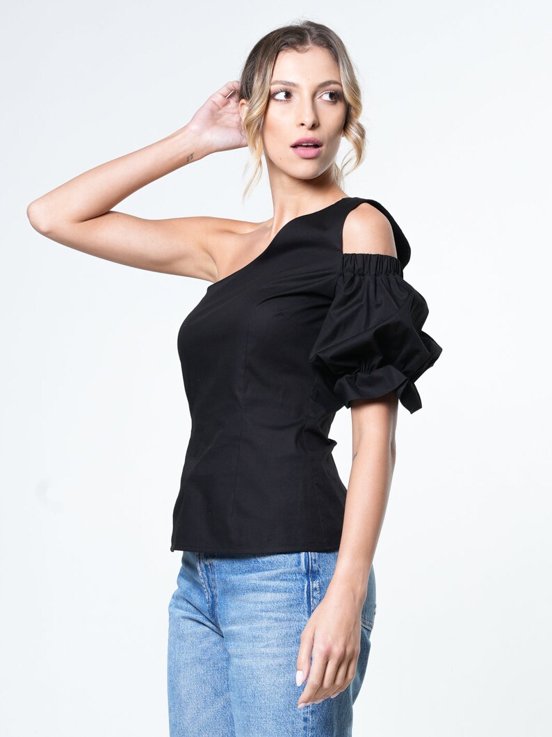 May include: A black one-shoulder top with a puff sleeve. The top has a fitted bodice and a relaxed fit through the body.