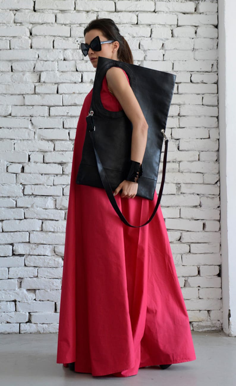 May include: A woman wearing a bright pink maxi dress and black sunglasses carries a large black leather tote bag with a silver strap.