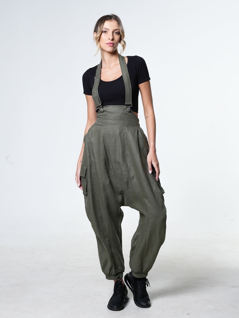May include: A woman wearing a black crop top and olive green linen overalls with suspenders. The overalls have a loose, baggy fit and feature a cargo pocket on the left leg.