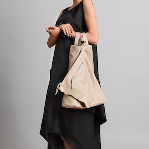 May include: A woman wearing a black sleeveless dress with a high low hemline and a beige leather bag. She is wearing black sneakers.