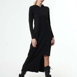 May include: A black long-sleeved hooded dress with a side slit and diagonal stitching detail. The dress is worn with black boots.
