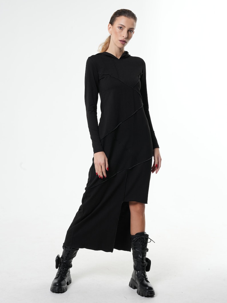 May include: A black long-sleeved hooded dress with a side slit and diagonal stitching detail. The dress is worn with black boots.