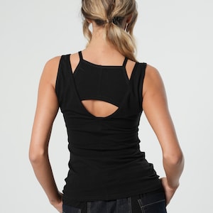 May include: Black sleeveless tank top with a cutout detail in the back. The tank top is made of a soft, stretchy fabric and has a fitted silhouette.