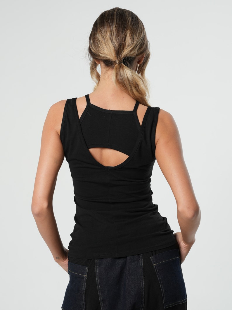 May include: Black sleeveless tank top with a cutout detail in the back. The tank top is made of a soft, stretchy fabric and has a fitted silhouette.