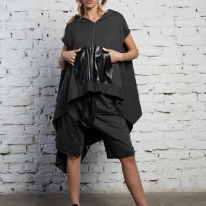 May include: A gray hooded top with a black leather pocket and a zipper closure. The top is styled with gray shorts and black sneakers.