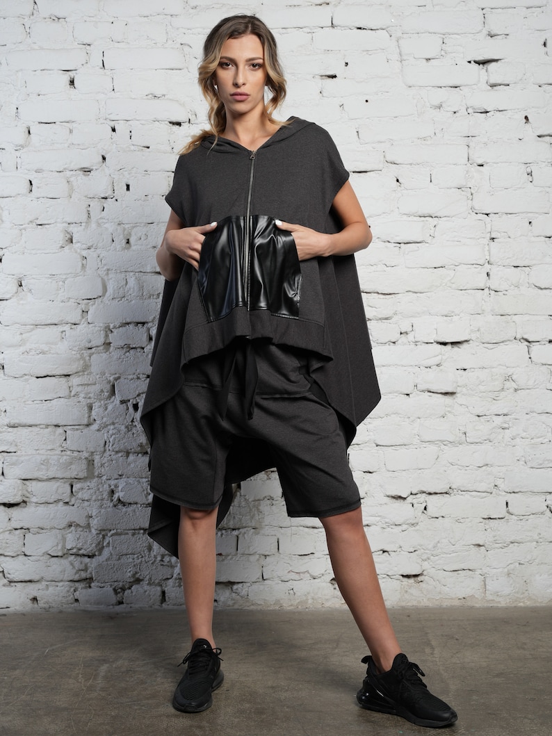 May include: A gray hooded top with a black leather pocket and a zipper closure. The top is styled with gray shorts and black sneakers.