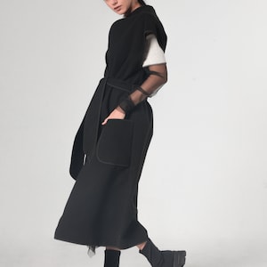 May include: A black sleeveless long vest with a belt and a large pocket. The vest is made of a soft, comfortable fabric and has a relaxed fit.