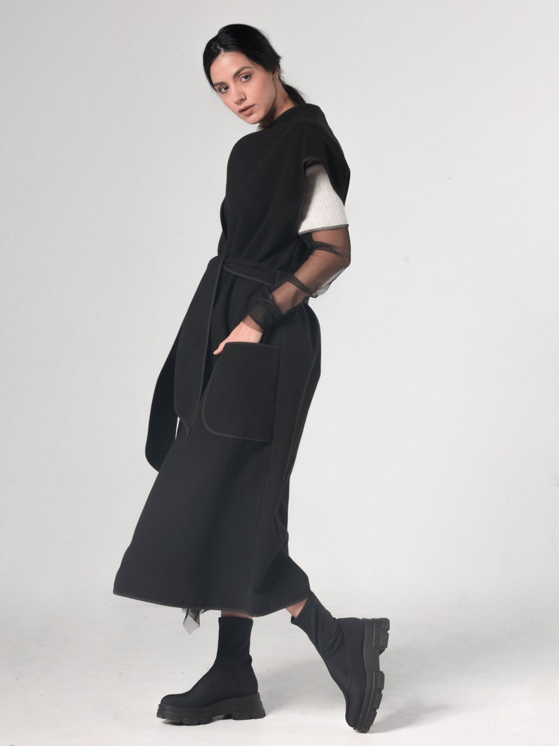 May include: A black sleeveless long vest with a belt and a large pocket. The vest is made of a soft, comfortable fabric and has a relaxed fit.