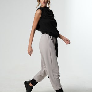 May include: A woman wearing a black sleeveless top with a cowl neck and grey pants. She is wearing black sneakers.