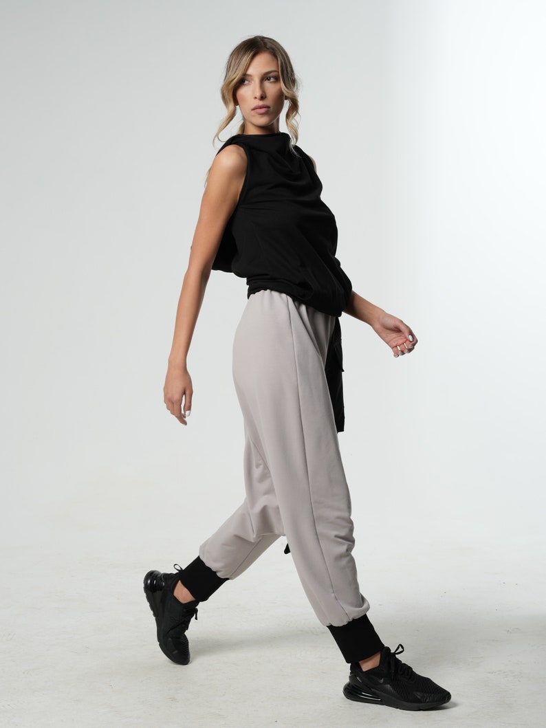 May include: A woman wearing a black sleeveless top with a cowl neck and grey pants. She is wearing black sneakers.